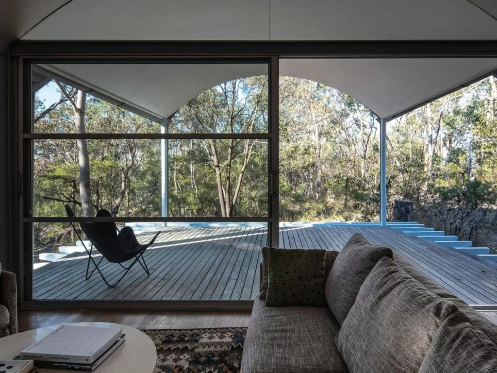 Interior view from a living room looking out through large glass sliding doors onto a wooden deck and forest.