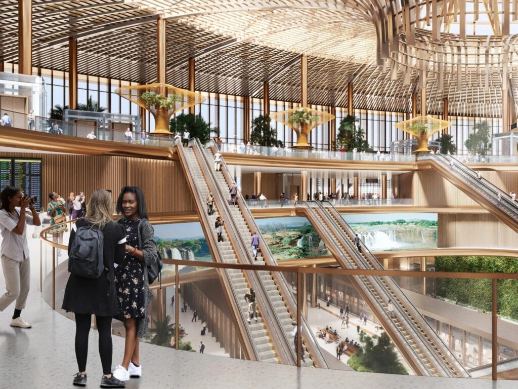 Interior view of Bishoftu Airport terminal showing multi-level concourses, escalators, and large digital screens displaying Ethiopian landscapes.