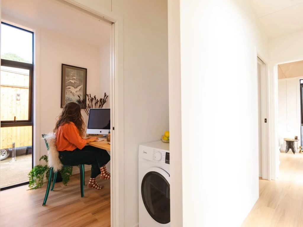 A woman working at a wooden desk in a dedicated small office nook next to an integrated laundry unit.