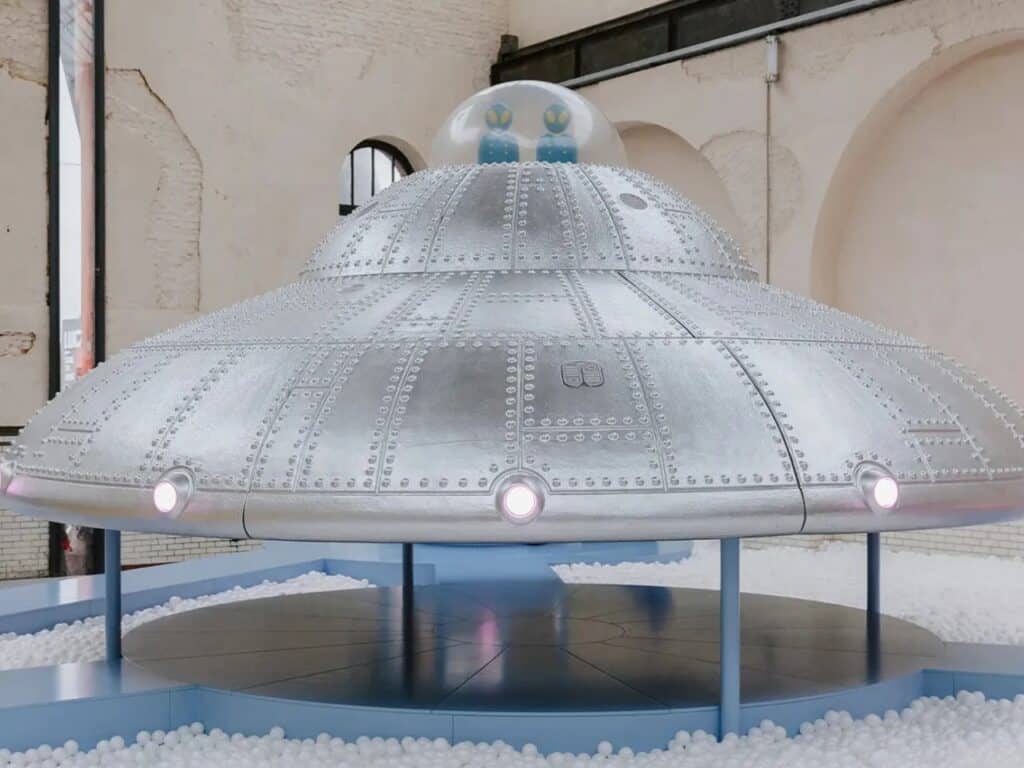 Close-up of a large silver metallic UFO structure with glowing lights, part of an interactive play environment.