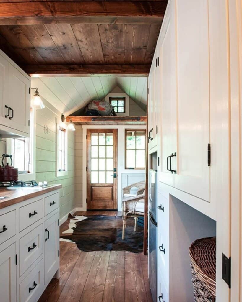 Interior view from the kitchen looking back toward the front door of the Ynez house, showing white cabinetry and a rustic area rug.