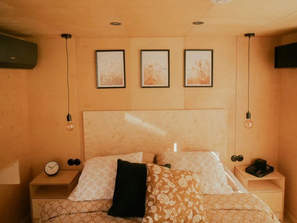 Cozy bedroom interior of Zenith tiny house with plywood walls, hanging light bulbs, and a minimalist bed setup.