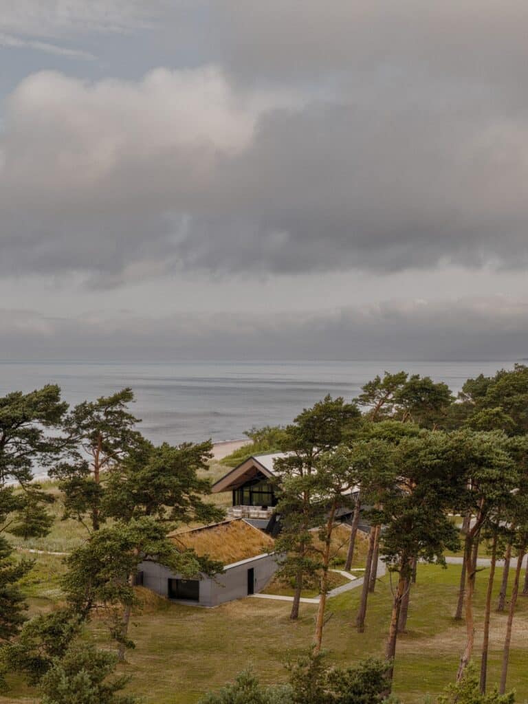 Aerial view of the SAR project residence and guest houses with grass-covered roofs nestled among pine trees by the Baltic coast.