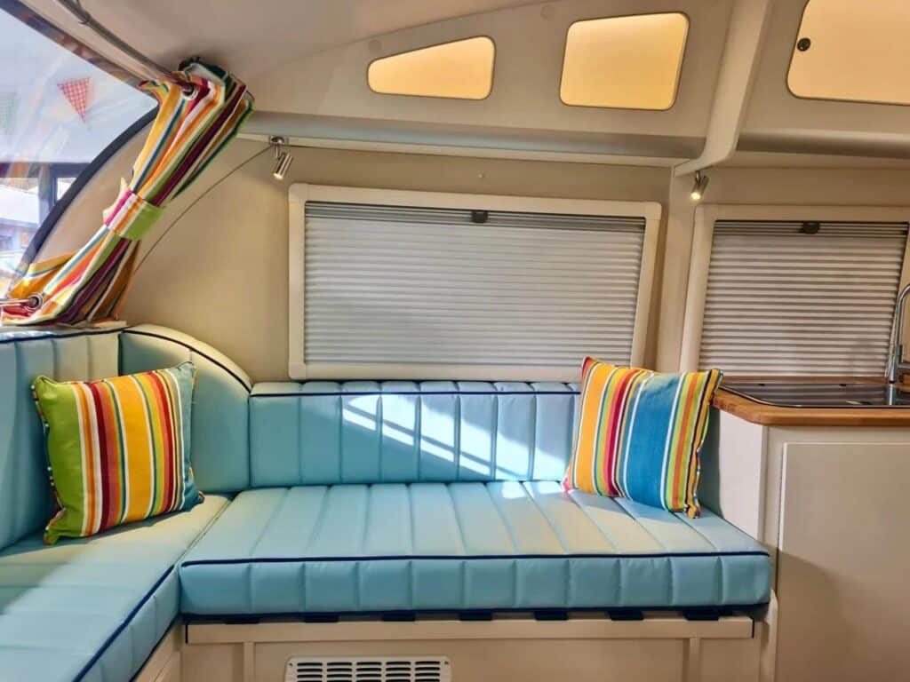 Side interior view of the Bothy caravan featuring blue padded benches, striped curtains, and integrated storage.