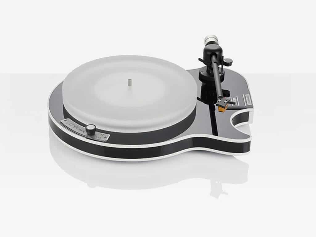 Top-down perspective of a black guitar-shaped turntable with a frosted platter on a white reflective surface.