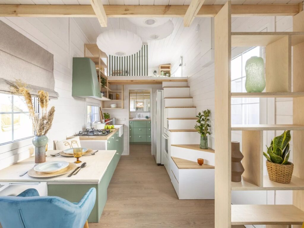 A view through the kitchen of a tiny house towards the stairs, showing integrated storage drawers within the staircase.