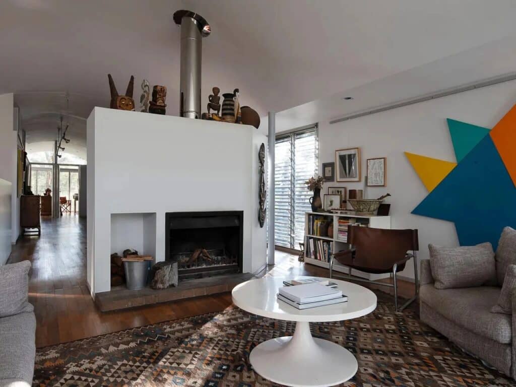 Modernist living room interior featuring a central fireplace wall decorated with tribal art and abstract paintings.
