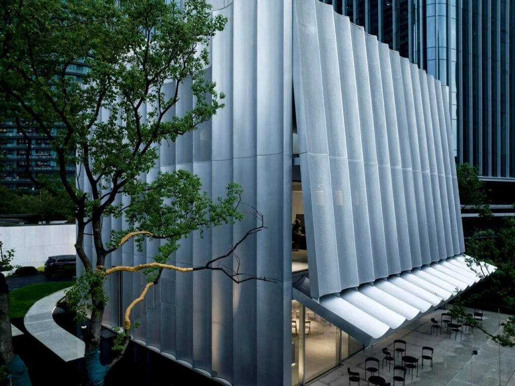 Wide angle exterior of Hangzhou Empathy Museum showing the integration with surrounding trees and the wave-like canopy.