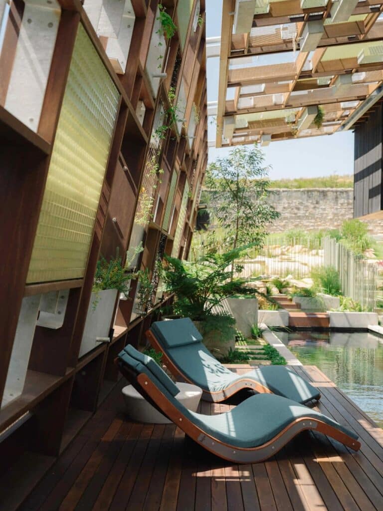 Close-up of ergonomic outdoor lounge chairs on a timber deck next to a natural pool and a vertical garden structure.