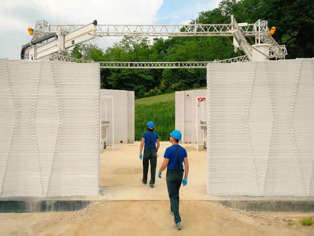 Two workers entering the 3D-printed farm structure through an arched opening, showing the interior courtyard.