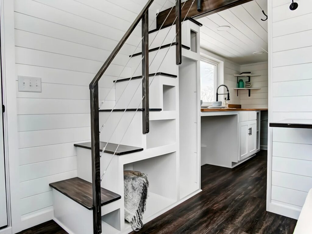 White stairs in a tiny house with built-in open cubby holes for storage leading up to a loft.