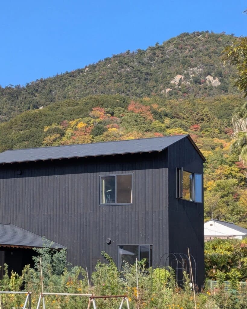 Rear view of Onomichi House showing large windows and a garden area, transitioning from a closed street facade to an open landscape view.
