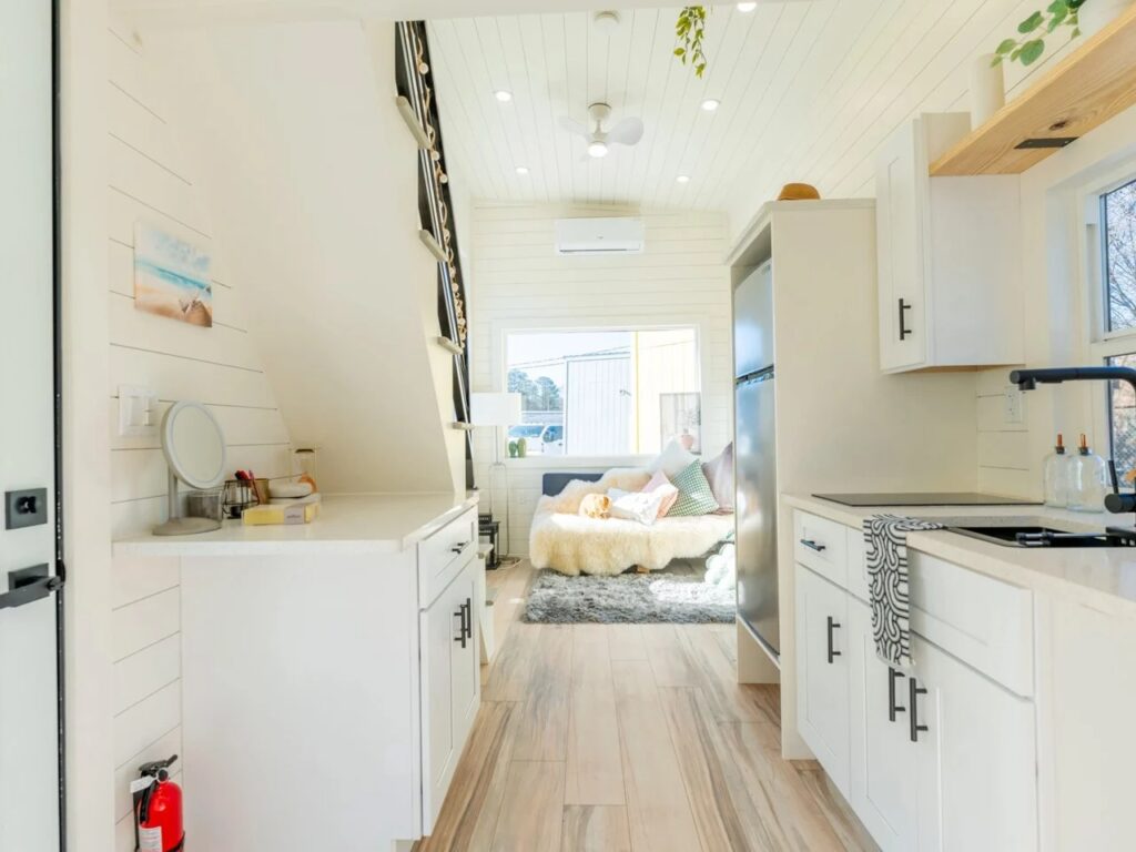 Wide interior view of the Sora 20 tiny home showing the flow between the workspace, kitchen, and living area.