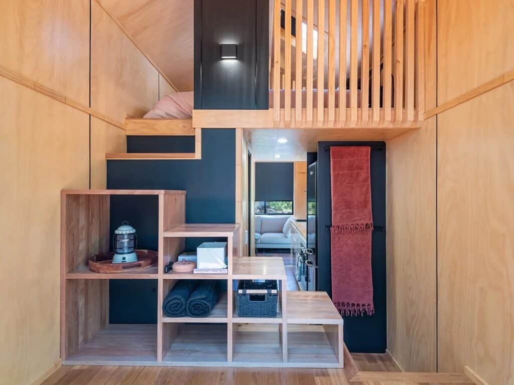 Interior view of the Artista tiny house showing a multifunctional wooden staircase with built-in storage leading to a sleeping loft.