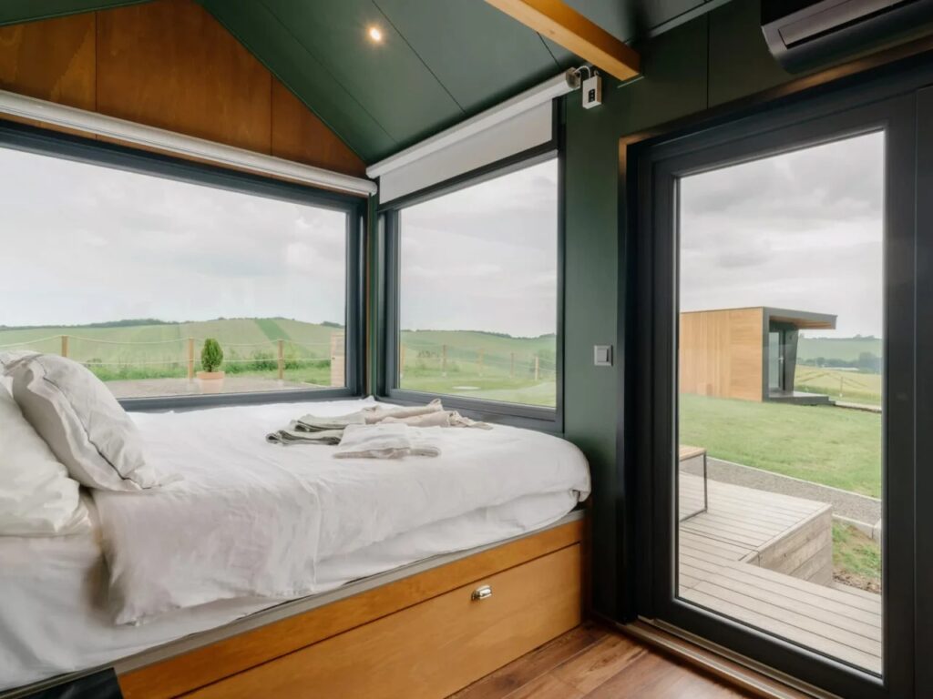 Interior view of the bedroom in Tiny Amsterdam with large windows overlooking a green field and a storage drawer under the bed.