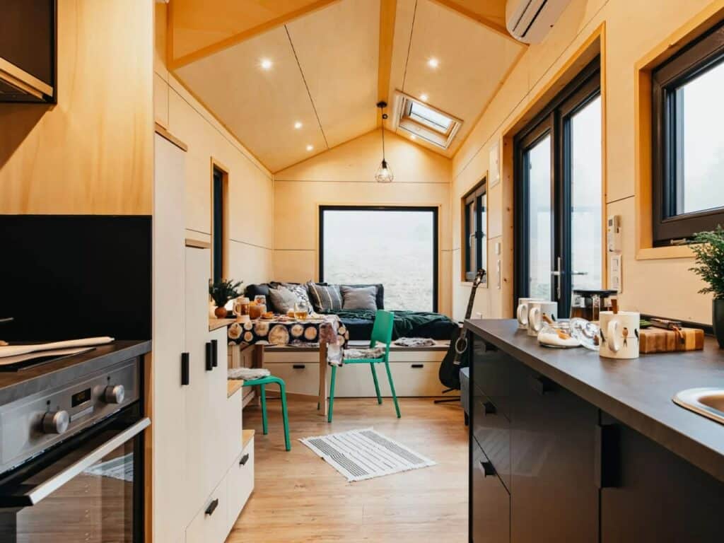 Perspective view from the kitchen of Tiny Hogwarts looking towards the living area, showing light wood interior panels and a skylight.