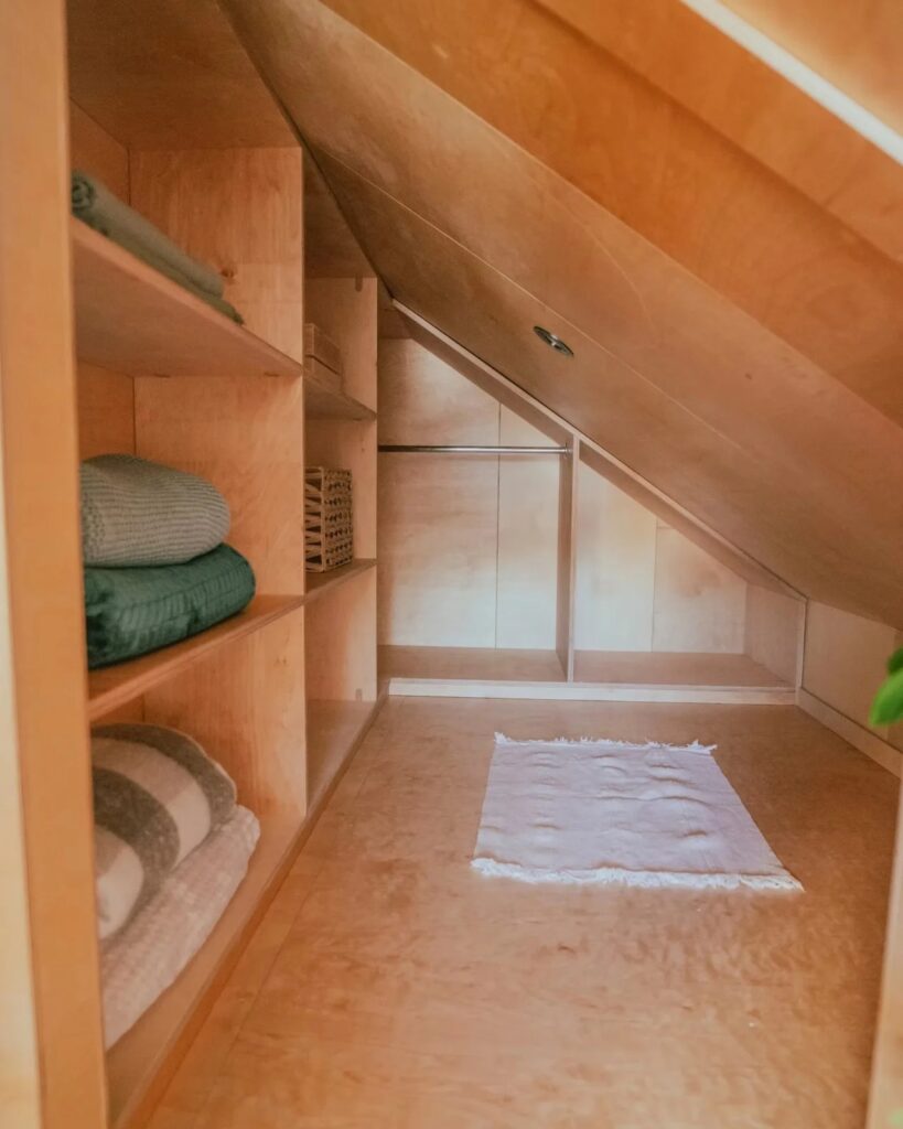Integrated wooden shelving and closet space built into the sloped walls of a tiny house.