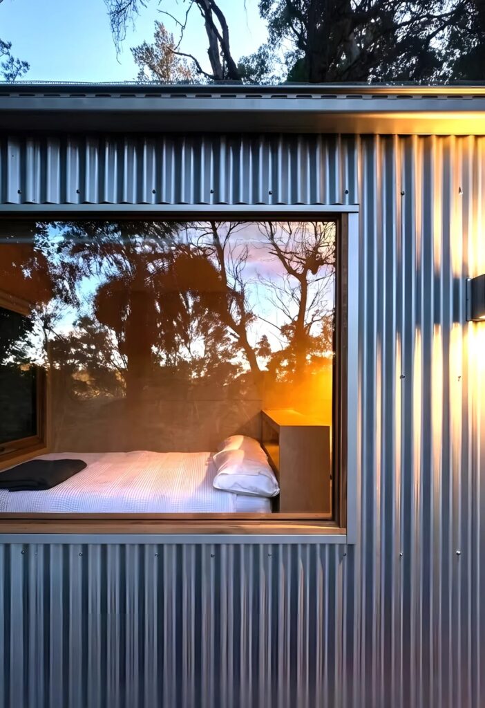 Close-up of the zinc corrugated facade reflecting the sunset, with a view of the bed through a large window.