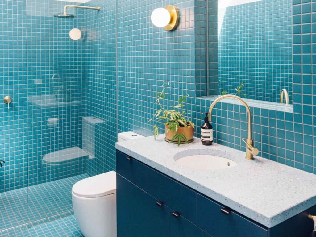 Modern bathroom with small blue mosaic tiles, a dark blue vanity with terrazzo top, and gold brass bathroom fixtures.