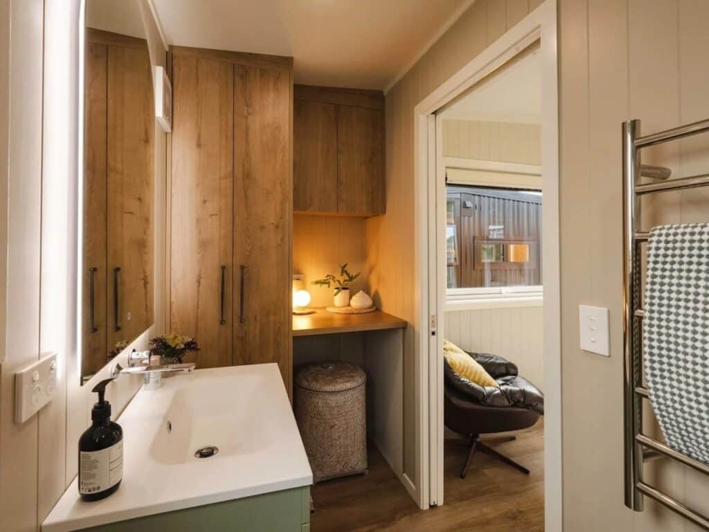 Modern bathroom vanity with a white sink, large backlit mirror, and custom wooden cabinets for integrated storage.