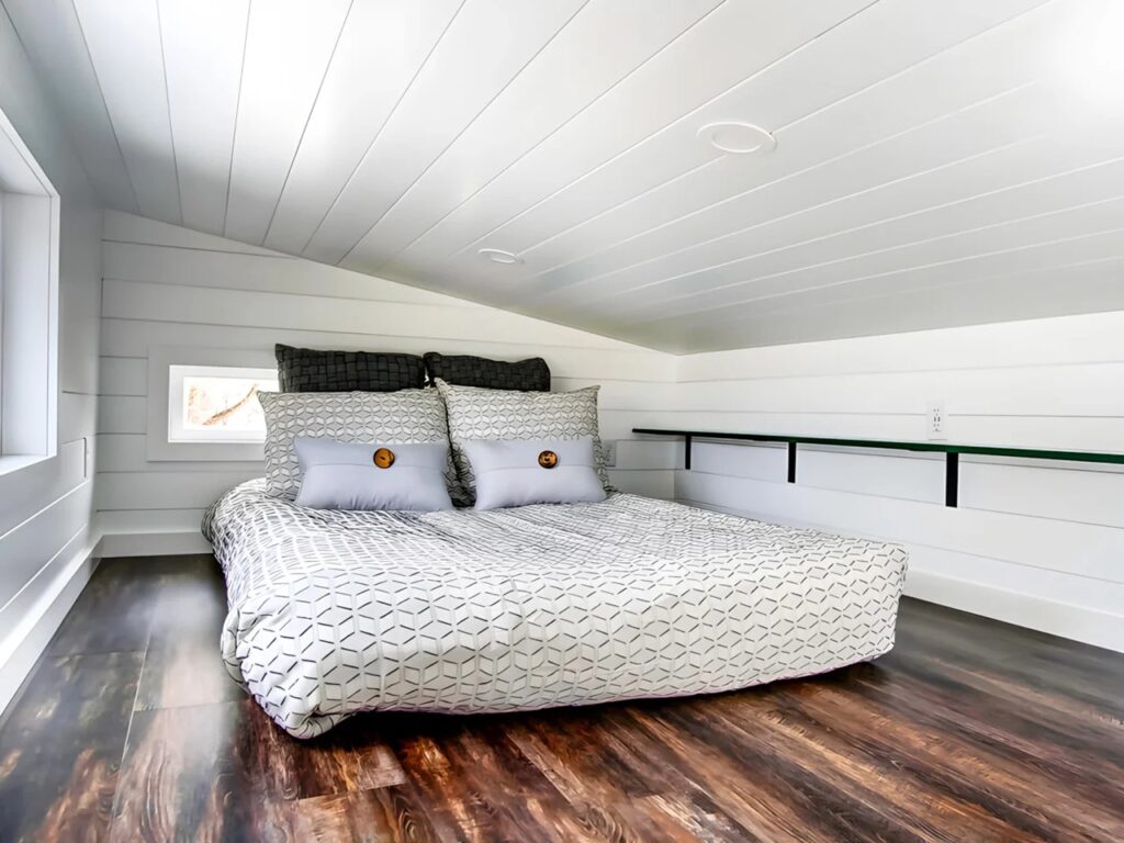 A cozy loft bedroom in the Kinnakeet house with a double bed, sloped ceiling, and white wood paneled walls.