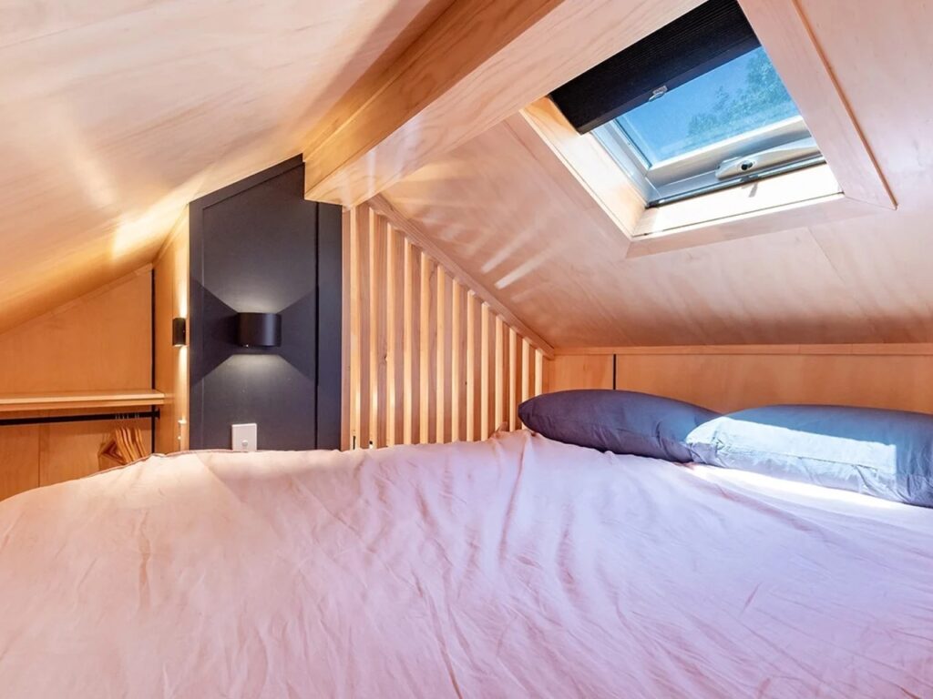 Close-up of the loft bedroom in the Artista tiny house with a double bed and a large skylight window for natural lighting.