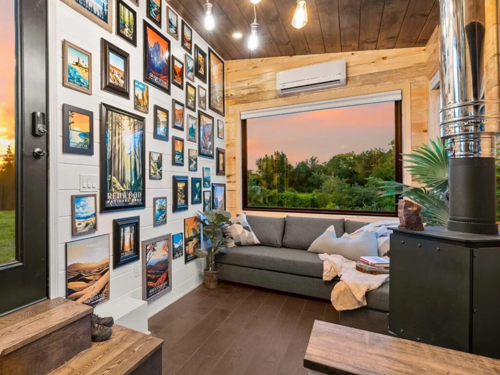 Cozy living room in a tiny house featuring a gallery wall of framed art, a large picture window, and industrial lighting.