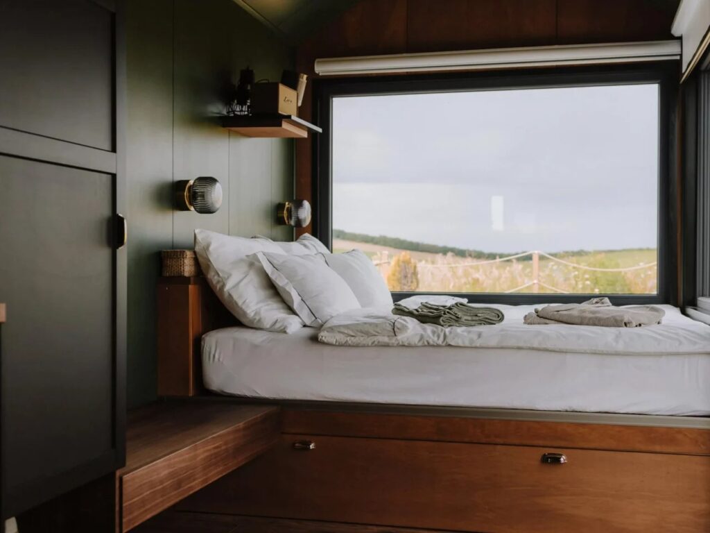 Minimalist bedroom interior with olive green walls, wooden accents, and a large view-port window.