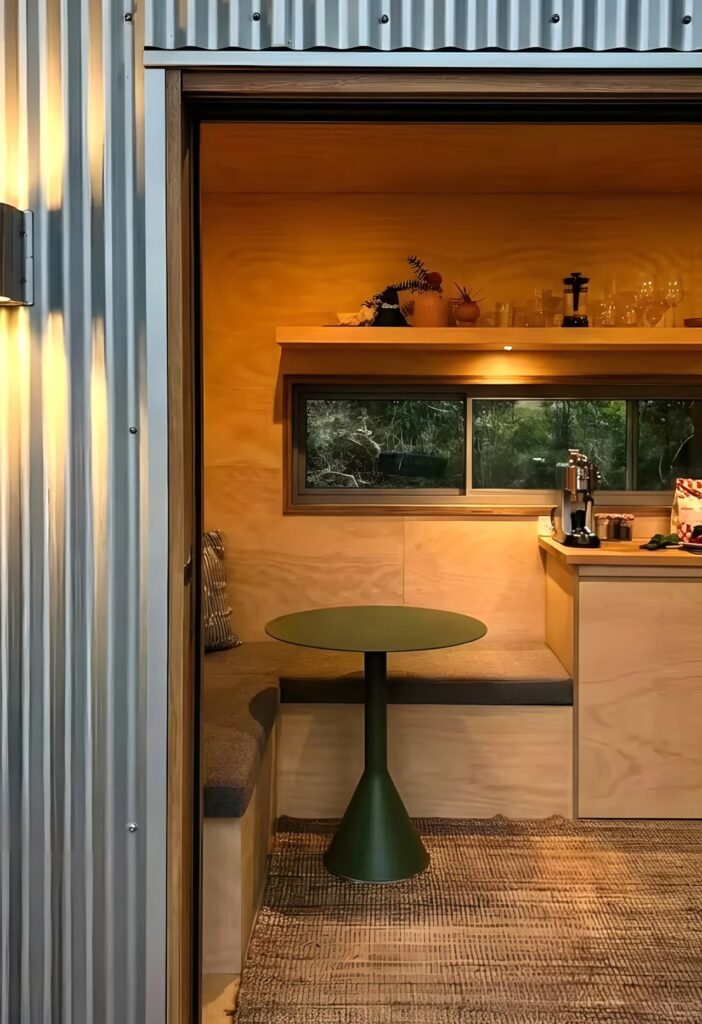 View through the sliding door into a compact dining area with a green pedestal table and plywood walls.