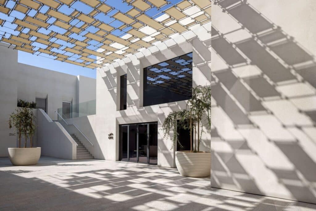 Bright white courtyard of Al Ain Museum cafe with desert plants in large pots and a modern sunshade structure.
