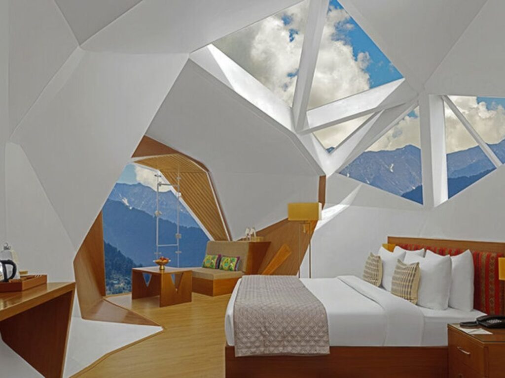 Luxury suite interior with a seating area, mountain view through an angled window, and minimalist wooden furniture.