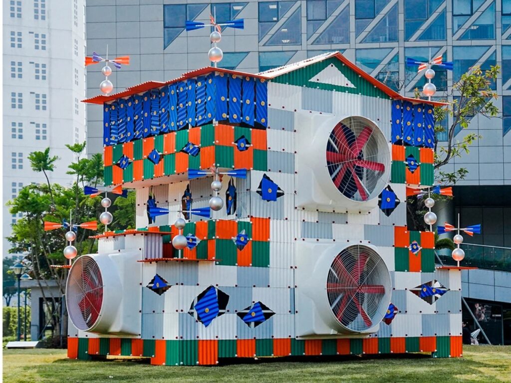 Three-quarter view of Clock House No. 2 showcasing its multi-layered facade, industrial fans, and vibrant color blocking in an outdoor setting.