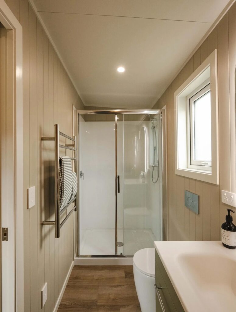 Compact bathroom interior with a glass-enclosed shower, wall-mounted toilet, and neutral-toned wall panels.
