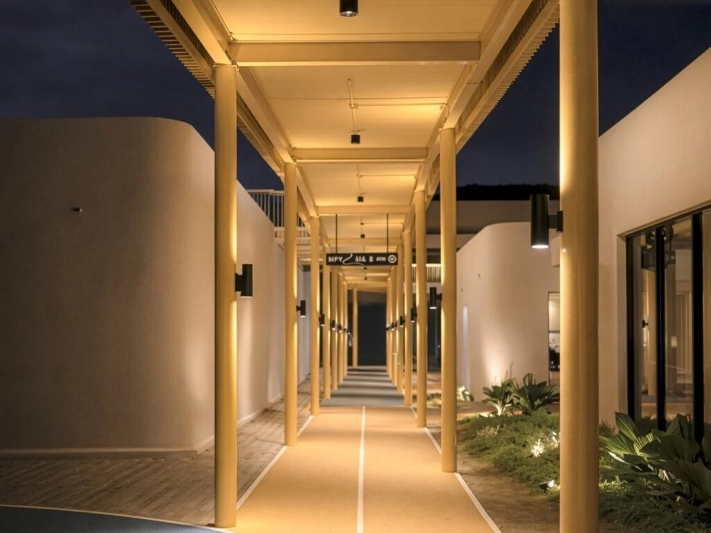 Night view of a long, illuminated yellow walkway supported by columns at My Front Yard project.