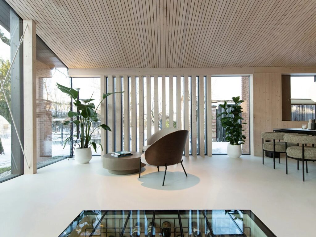 Interior view looking out through large windows with vertical wooden louvers and indoor plants.