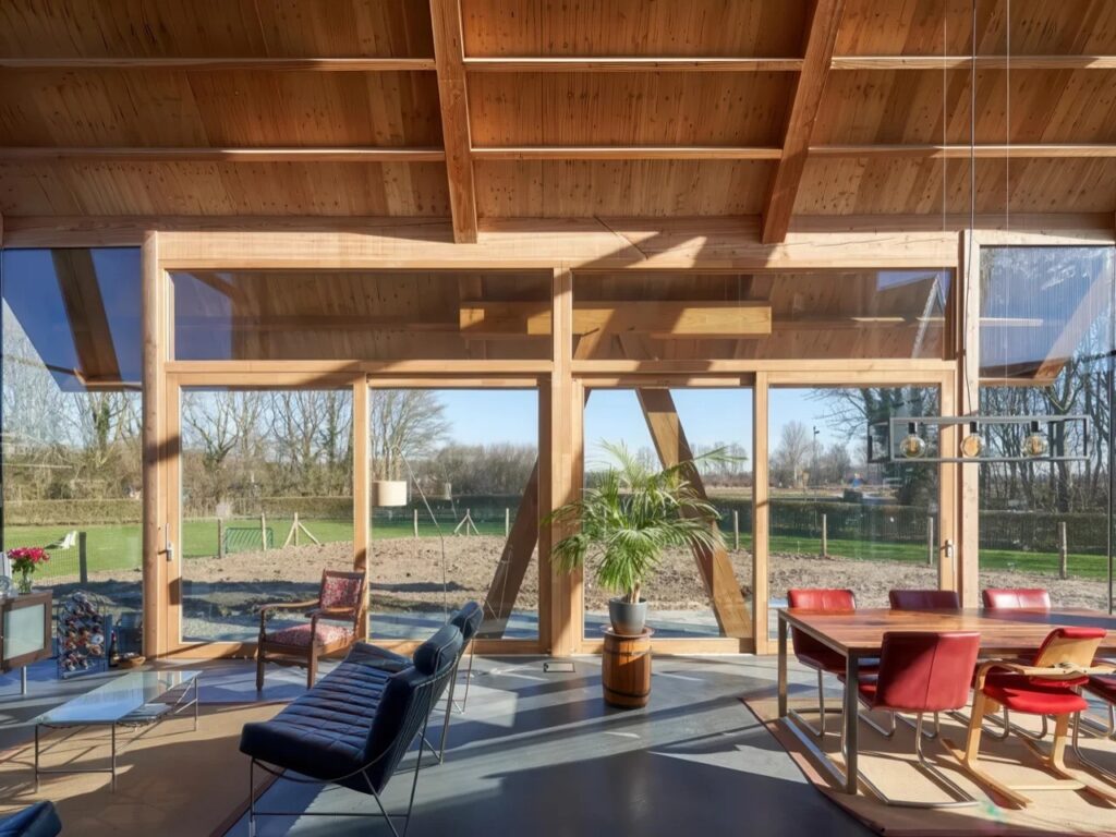Bright living room with floor-to-ceiling windows and visible wooden roof rafters in a modern Dutch barnhouse.
