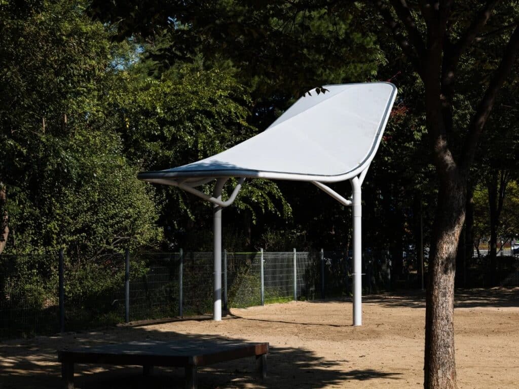 A single white Seoul Wing structure standing in a sandy playground area, illustrating the neutral color palette.