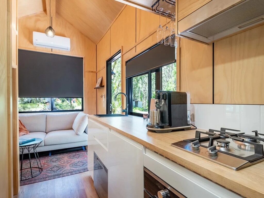 Modern compact kitchen in the Artista tiny house featuring a gas stove, coffee machine, and view of the living area.