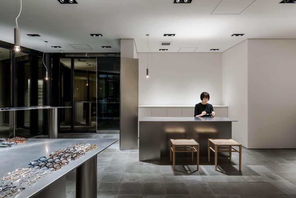 Staff member interacting with a customer at a minimalist grey service counter in Ashiya Optical Store.