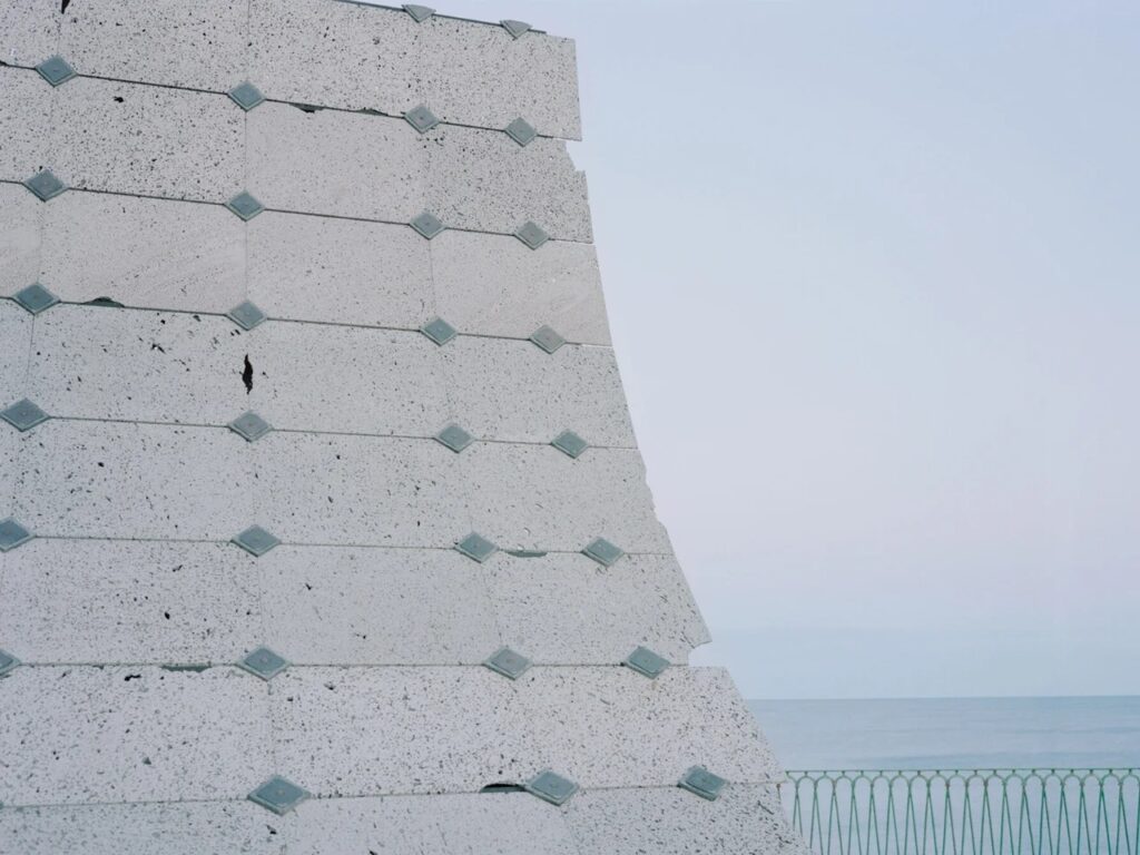 Extreme close-up of a lava stone roof panel with square metal fasteners against a clear sky.