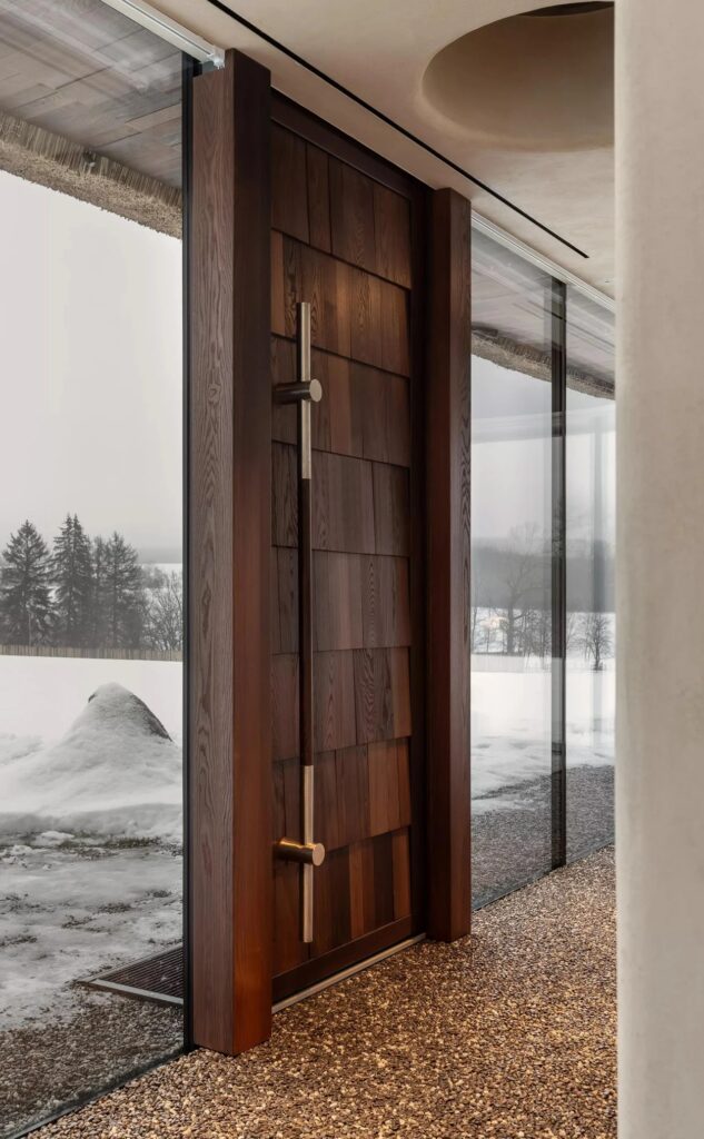 Close-up of a tall, dark textured wooden door with a sleek metallic handle integrated into a glass wall.