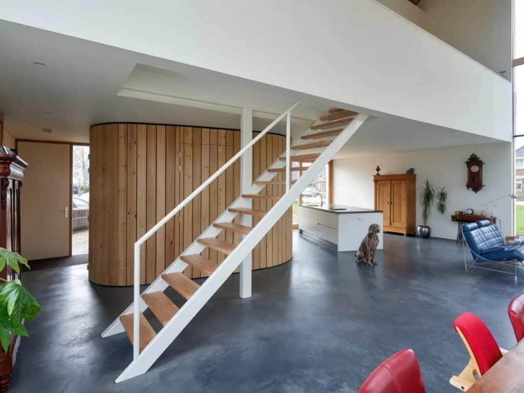 Interior view featuring a white staircase and a large curved wooden wall used for spatial organization.