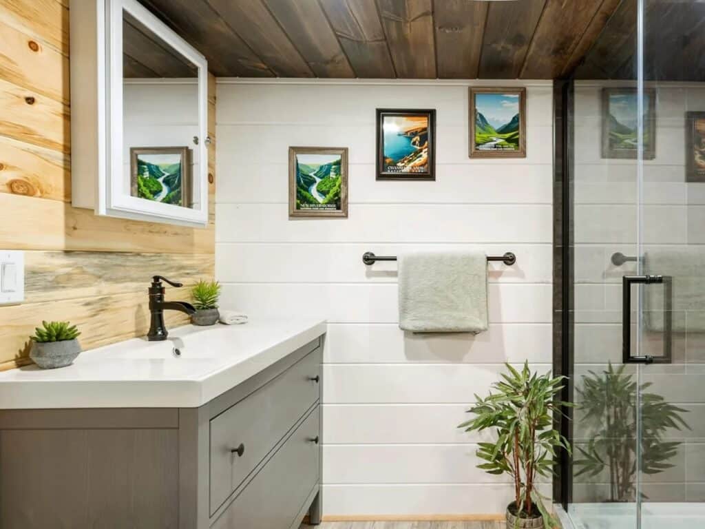Modern tiny home bathroom featuring a gray vanity, white shiplap walls, and a glass-enclosed walk-in shower.