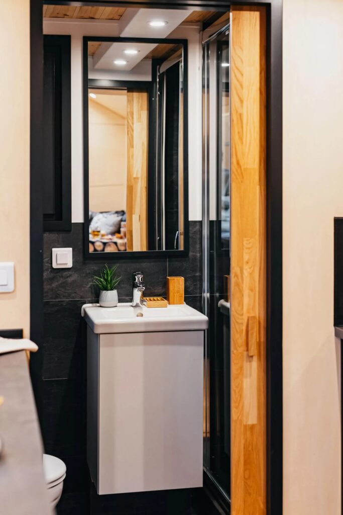 Compact bathroom design in a tiny house with a minimalist white sink, dark slate tiles, and a sliding wooden door.