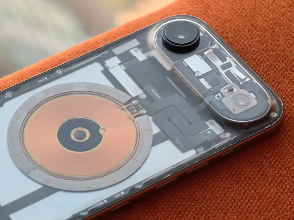 A modified transparent iPhone lying flat on an orange textured surface, showing the Apple logo over internal parts.