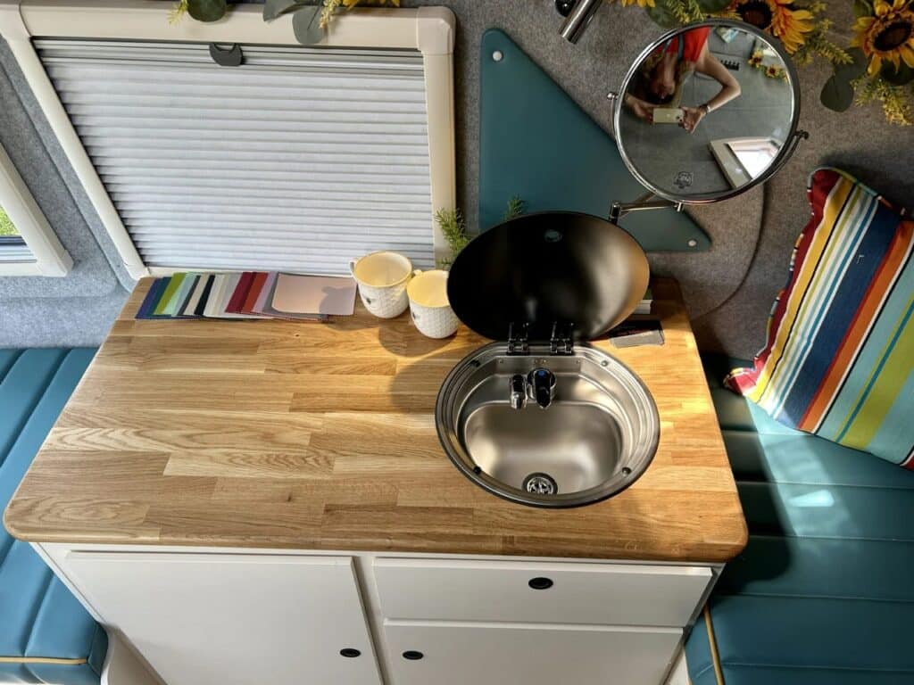 Top-down view of a wooden countertop in the Bothy caravan with a small round sink and accessories.