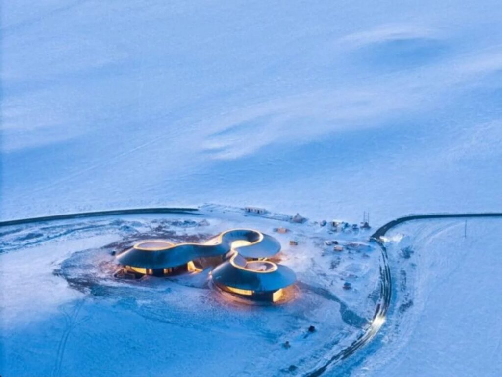 The Volcano Visitor Center illuminated at night, glowing against the vast blue snowy plains of Northern China.