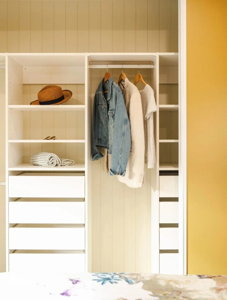 Built-in white wardrobe system in a tiny house bedroom with organized shelves, drawers, and hanging space.