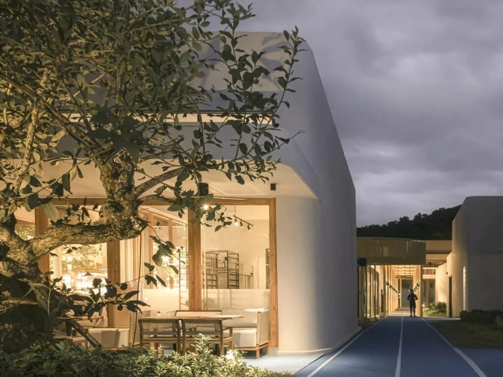 View of a cozy cafe interior through a large glass window, framed by a tree in the foreground at My Front Yard.