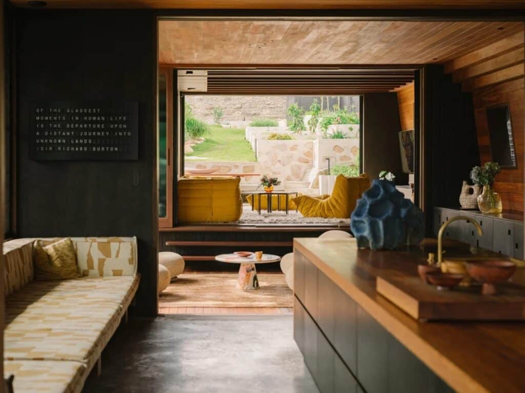 Interior view looking out towards a tiered stone garden and yellow lounge seating, showcasing the indoor-outdoor transition.